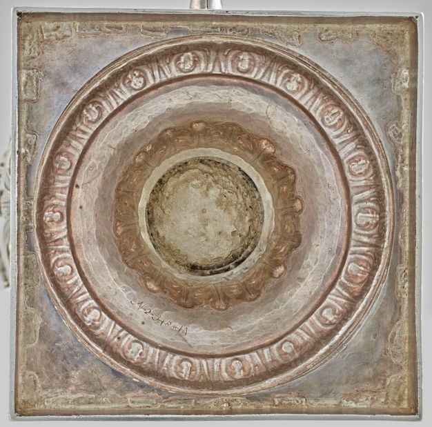 Square base of a silver vessel enclosing six circles of ornamentation with varying levels of wear.