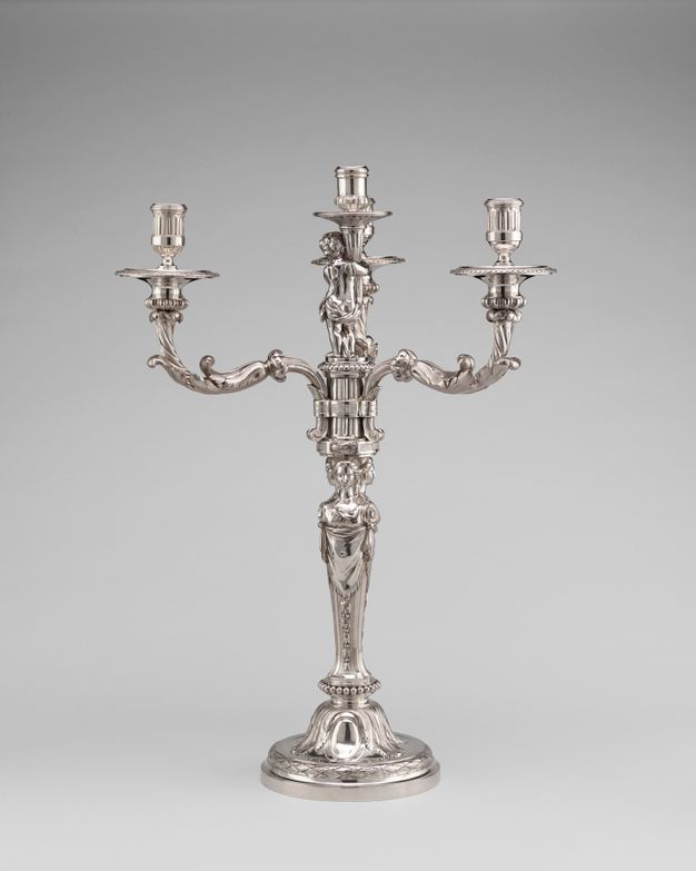 Back view of a girandole with four candelabra styled as leafy branches protruding from a base held up by three women standing back to back.