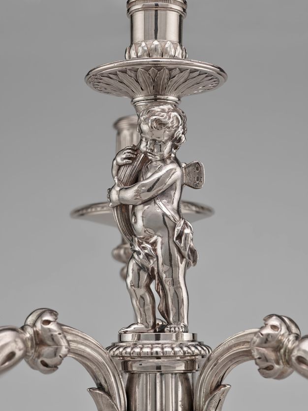 Close-up of the putto holding a branch that leads up to a drip pan and candle cup.