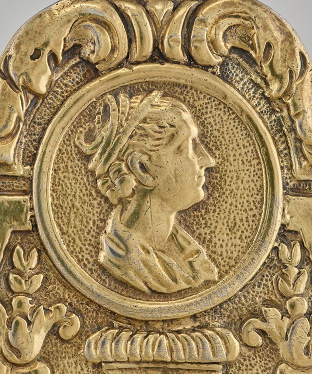 Profile of a woman with a coiled headpiece on her updo framed by a circle and leafy decorations.
