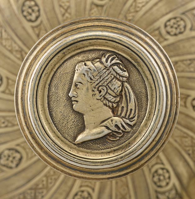 Top-view of the lid's knob featuring the profile of a woman with her hair braided into a bun and a veil cascading from her bun to her neckline.