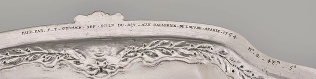 Close-up of the inscription underneath the edge of the stand, revealing the artist's signature, the numeral, and weight of the stand above a garland decoration.