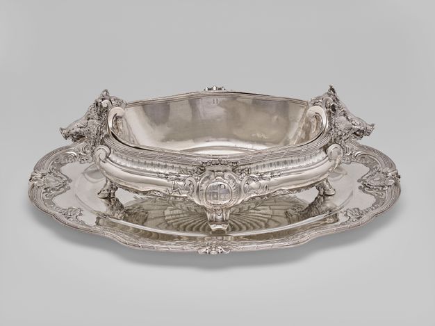 Oval tureen with boar heads and hooves at each end and a coat of arms on each side.