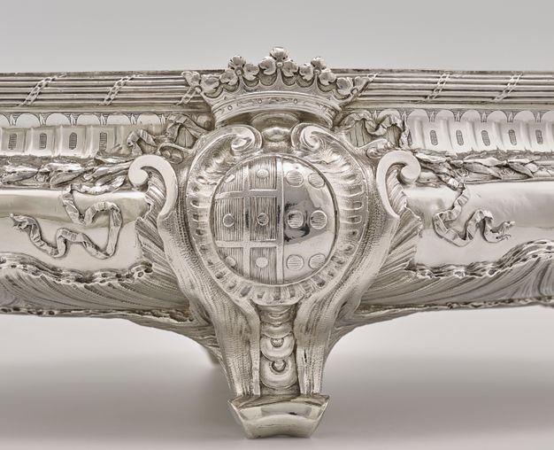 Coat of arms topped with crown and surrounded by ribbons and pleated fabric.