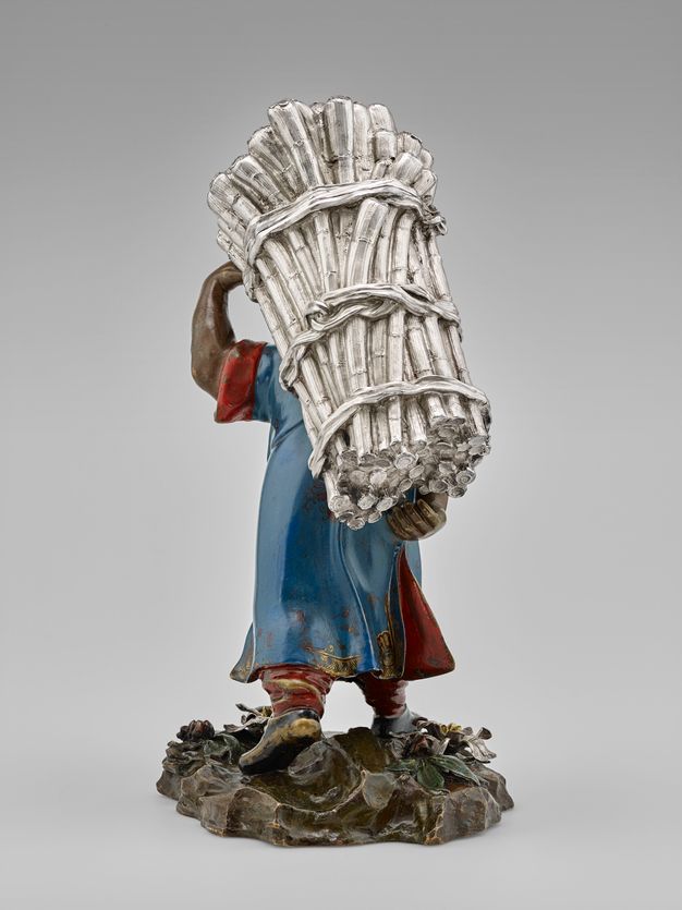 Field laborer bent from the weight of silver-colored sugarcane stalks.