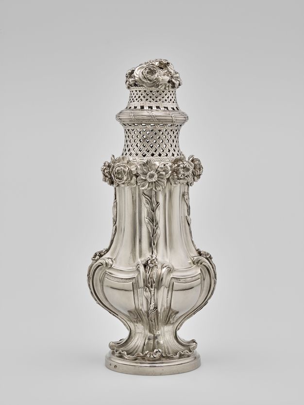 Silver sugar caster with a wide leafy base, flowers rising up its body, and two woven baskets with flowers on top.