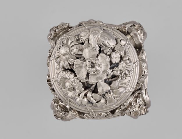 Top view of the silver sugar caster with one large flower surrounded by many types of smaller flowers on the lid.