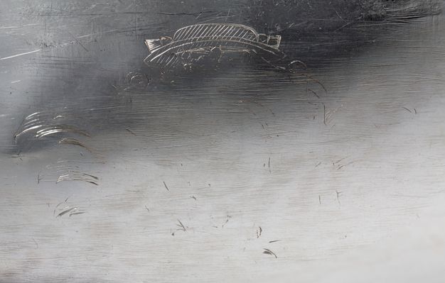 Close-up of a faded engraving of a hat framed by palm fronds and a coronet.