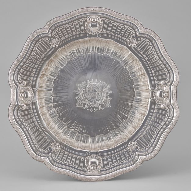 Top view of a flower-shaped stand decorated with wreaths along the edge and a coat of arms at its center.