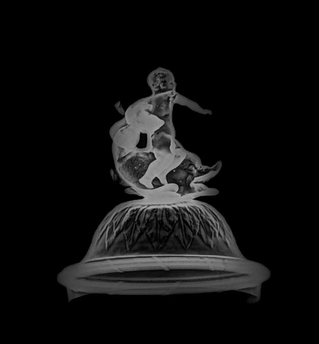Close-up of an x-radiograph of a fountain's lid, showing the side profile of a adolescent holding a shell and wrestling a dolphin.