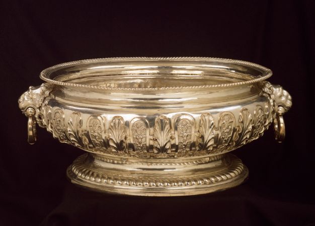 Large gold cistern decorated with round arches enclosing leaves and branches with two handles held by lions' heads.