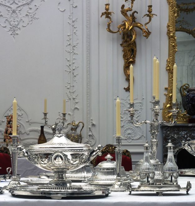 Close-up of a place setting with a candelabra standing beside a girandole and a lidded tureen and stand.