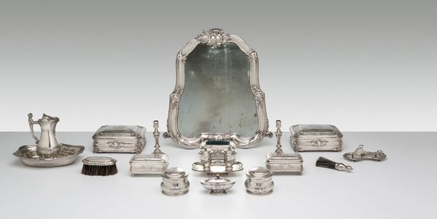Silver toilette set with nineteen pieces, including a pitcher, jewelry boxes, hair brush, candelabra, and a mirror.