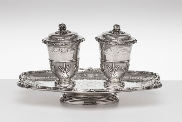 Set of two lidded beakers decorated by palm fronts on a raised stand.