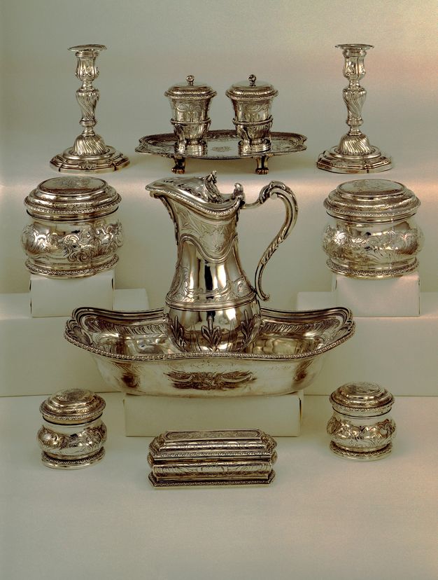 Silver toilette set with a pitcher, basin, a variety of lidded vessels, candelabra, and a two lidded beakers on a tray.