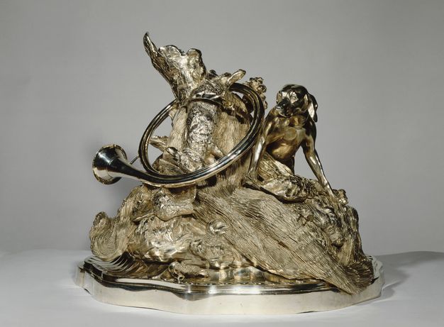 Centerpiece featuring a dog perched on a tree trunk surrounded by curling foliage and topped by a hunting horn and dead rabbit.