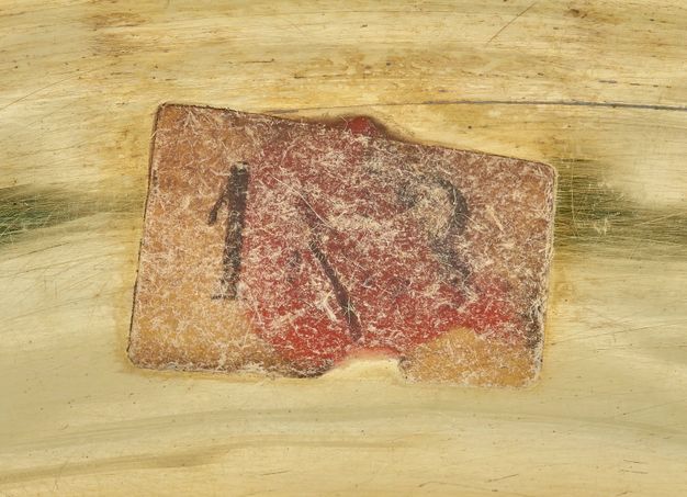 Close-up of a yellowed tag with the numbers 1[8]3 stained red by the wax adhesive.
