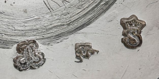 Close-up of two interlaced Ls, the initials RJA, and a crowned S, from left to right, stamped on the girandole.