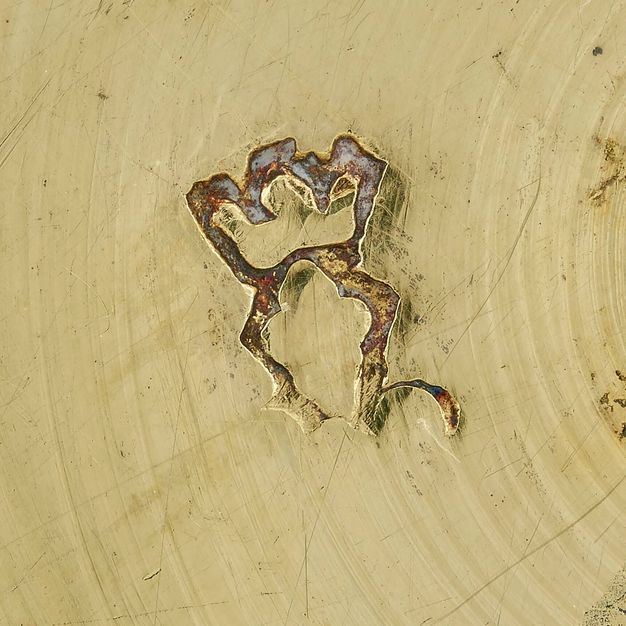 Close-up of a crowned fleur-de-lys partially stamped on the bowl's lid, missing definition on the bottom half of the design.