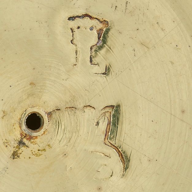 Close-up of the letters L and R partially stamped on the bowl's lid, missing definition on the left side of each letter.