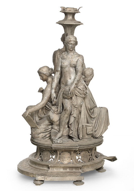 Metallic sculptural base for a candlestick with a broken frieze on the foot and four nude and draped female figures, two of whom are standing while the other two are seated.