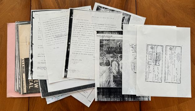 Documents arranged in an overlapping pile on a table surface, photographed from above. Only parts of each are legible.