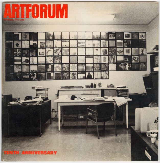 Cover showing a full-bleed black-and-white photograph of an office space with perpendicular desks cluttered with objects under fluorescent lighting. A chair is pushed back from one of the desks, and the back wall displays cover images hung together in a rectangular grid pattern.