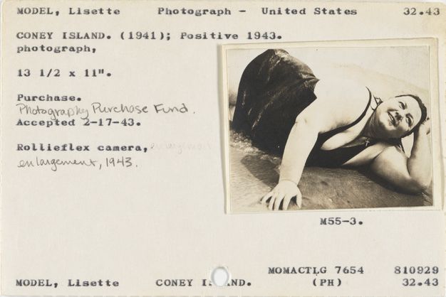 Typewritten card bearing a small print of a smiling, full-figured model in a swimsuit lying on her side with her arm holding up her head as water laps the sand beneath her. Handwritten annotations in pencil note “Photography Purchase Fund” and “Enlargement, 1943.”