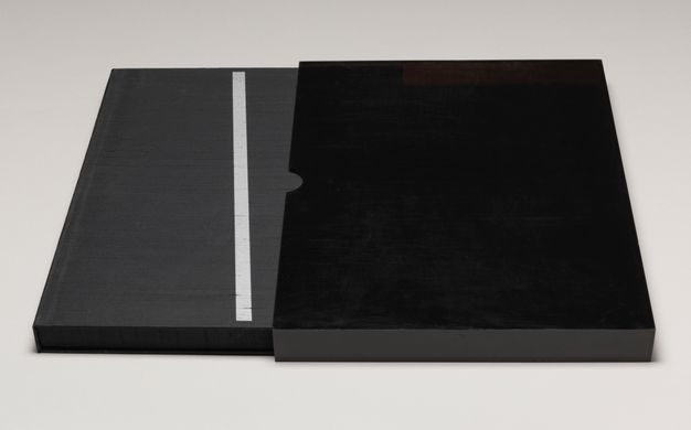 The enclosed portfolio on a flat surface mostly pulled out of the slipcover toward the viewer’s left, revealing its silkscreened line.