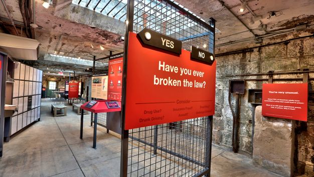 A graphic panel in red, mounted on a wire mesh partition dividing the room, invites the viewer to consider kinds of lawbreaking; arrows bearing the words “yes or “no” direct the viewer to one side of the exhibition space or the other.