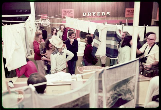 Artworks, clipped to a clothesline, zigzag across a laundromat, in which crowds of visitors gather.
