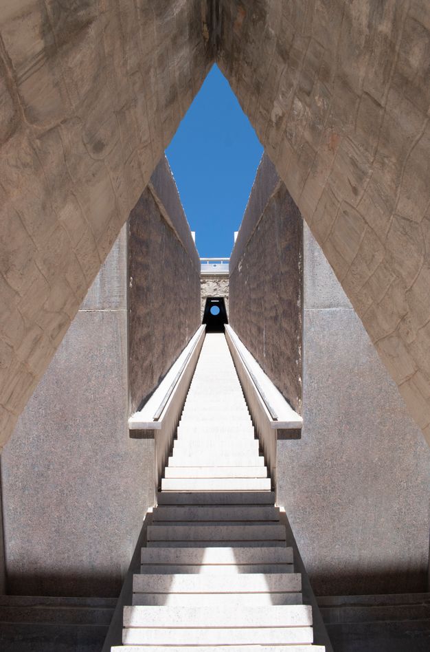 Viewed through a triangular opening featuring a blue sky, a long staircase called the Star Tunnel leads to a round aperture at the top.