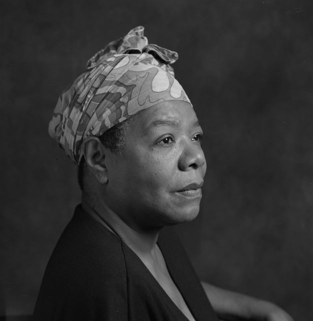 A woman looks off to the distance in this black-and-white headshot. With her hair wrapped in a colorful scarf, she embodies a regal sense of self reflection and presence.