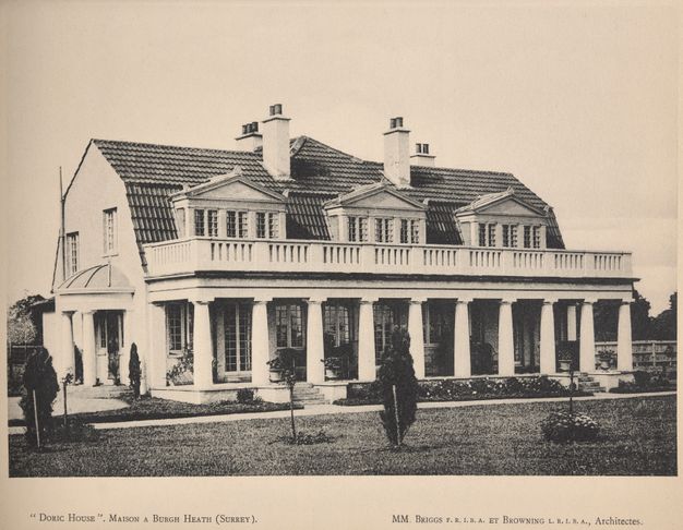Black-and-white photograph of a two-story house. The exterior features Doric columns, a covered veranda, and an upper floor balcony with patio doors and windows housed in classical temple facades.
