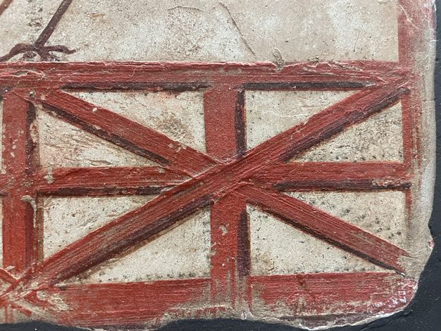 Mural detail depicting a red lattice, in which small black dots can be seen along the outline of the crisscrossed bars.