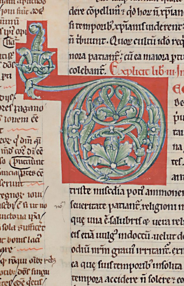 A green foliate initial outlined in blue, within a red background.