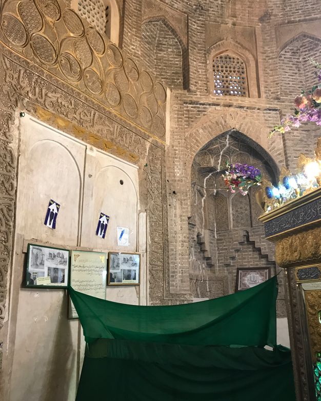 Interior with a wall of smooth white plaster, a piece of green fabric hung for separation, and an arched corner niche.