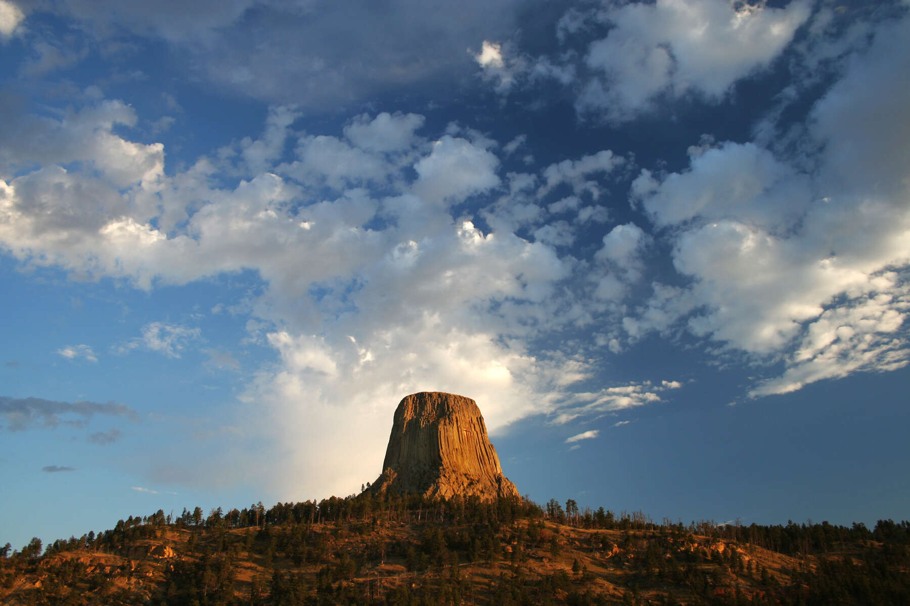 Striking view of an isolated hill with steep vertical sides and a flat top with vivid clouds in the back.
