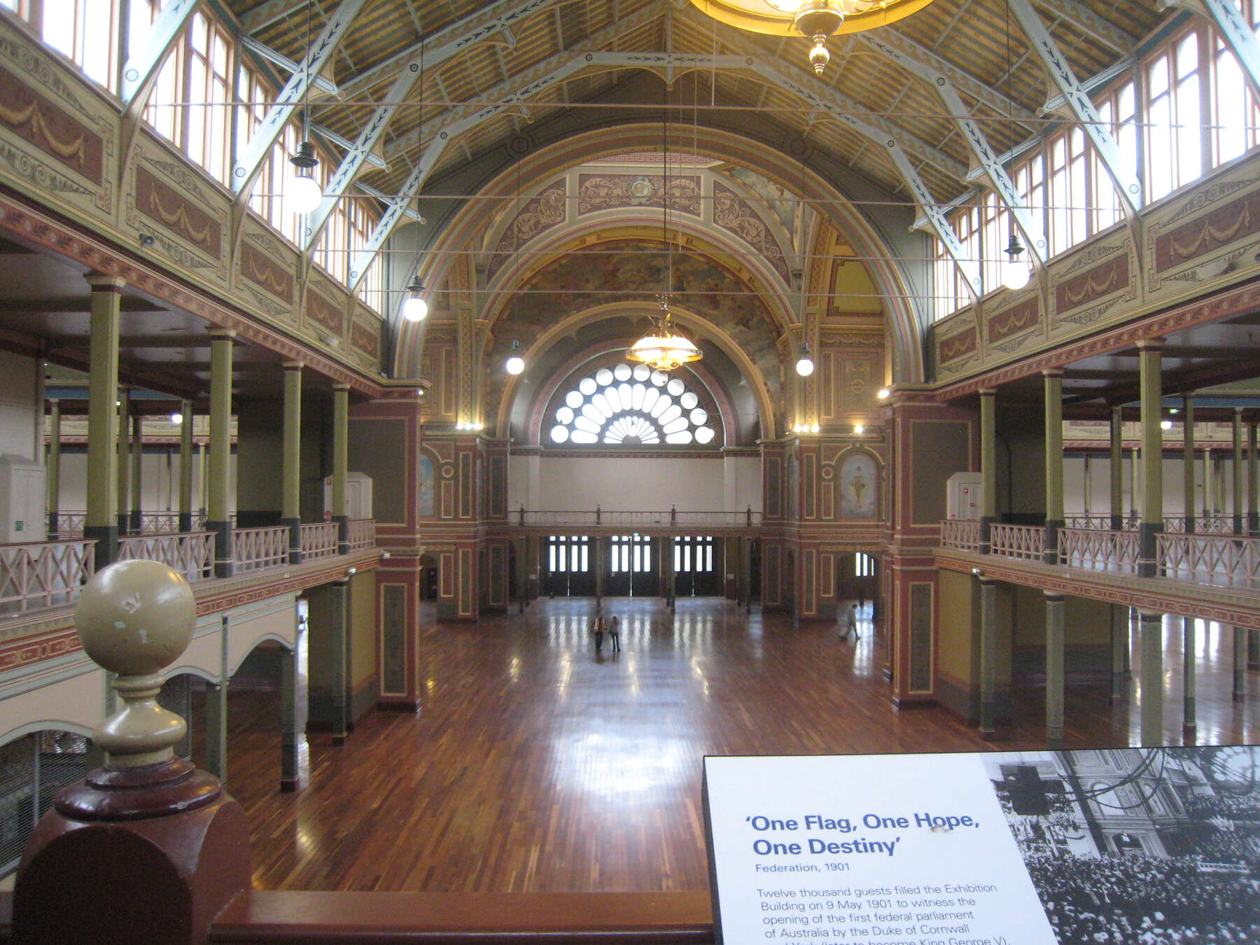 Colorfully painted, two-story palace hall with open balconies and massive arched doorways in the back near the main entrance.