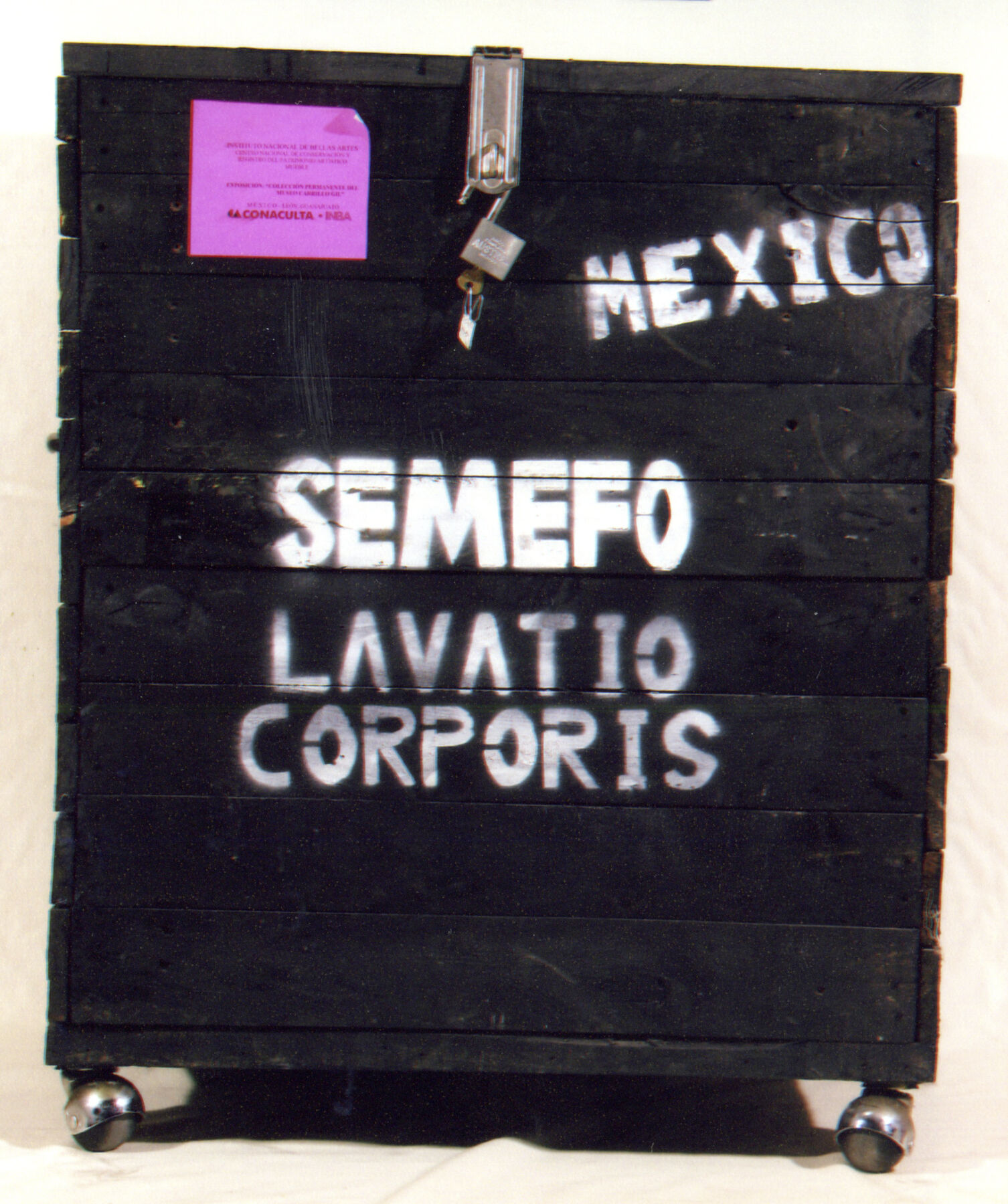 A black box with bright magenta sticker on the left and white bold lettering that says Mexico in the right corner and Semefo, Lavatio Corporis in the middle
