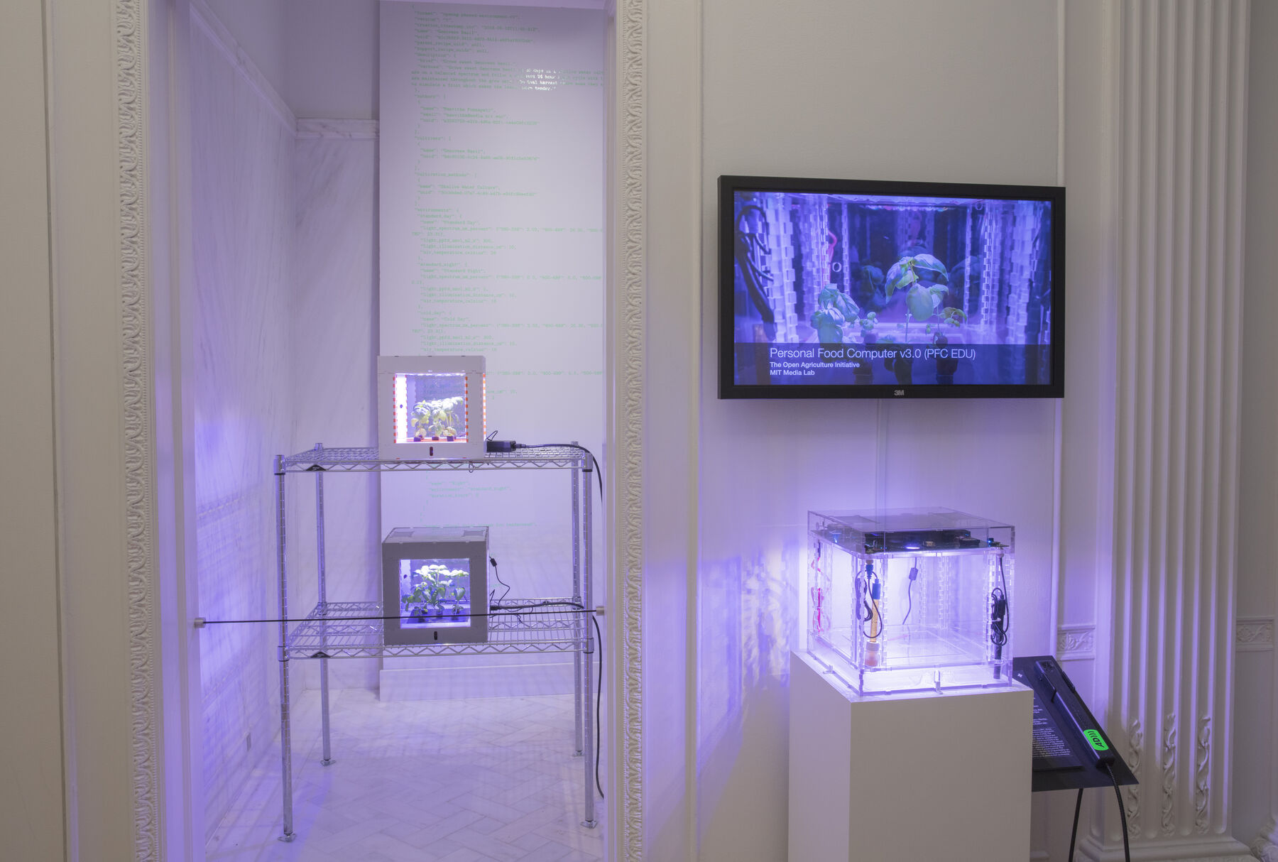 A white room with dim purple lights with a T.V mounted on the entrance displaying the white cube garden chambers found througout the room