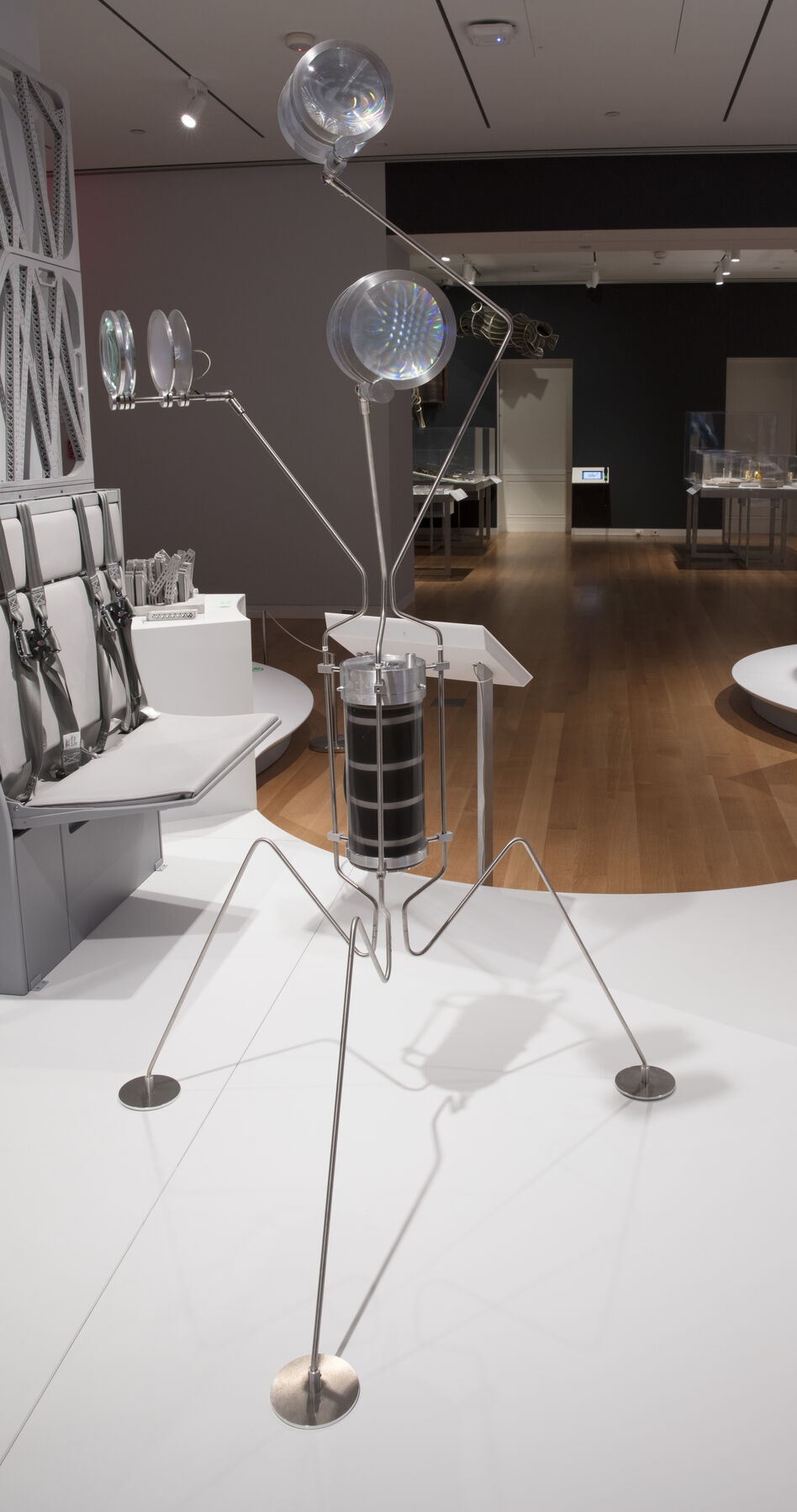 A metal sculpture with three legs with a container in the middle that attaches to three circular lights