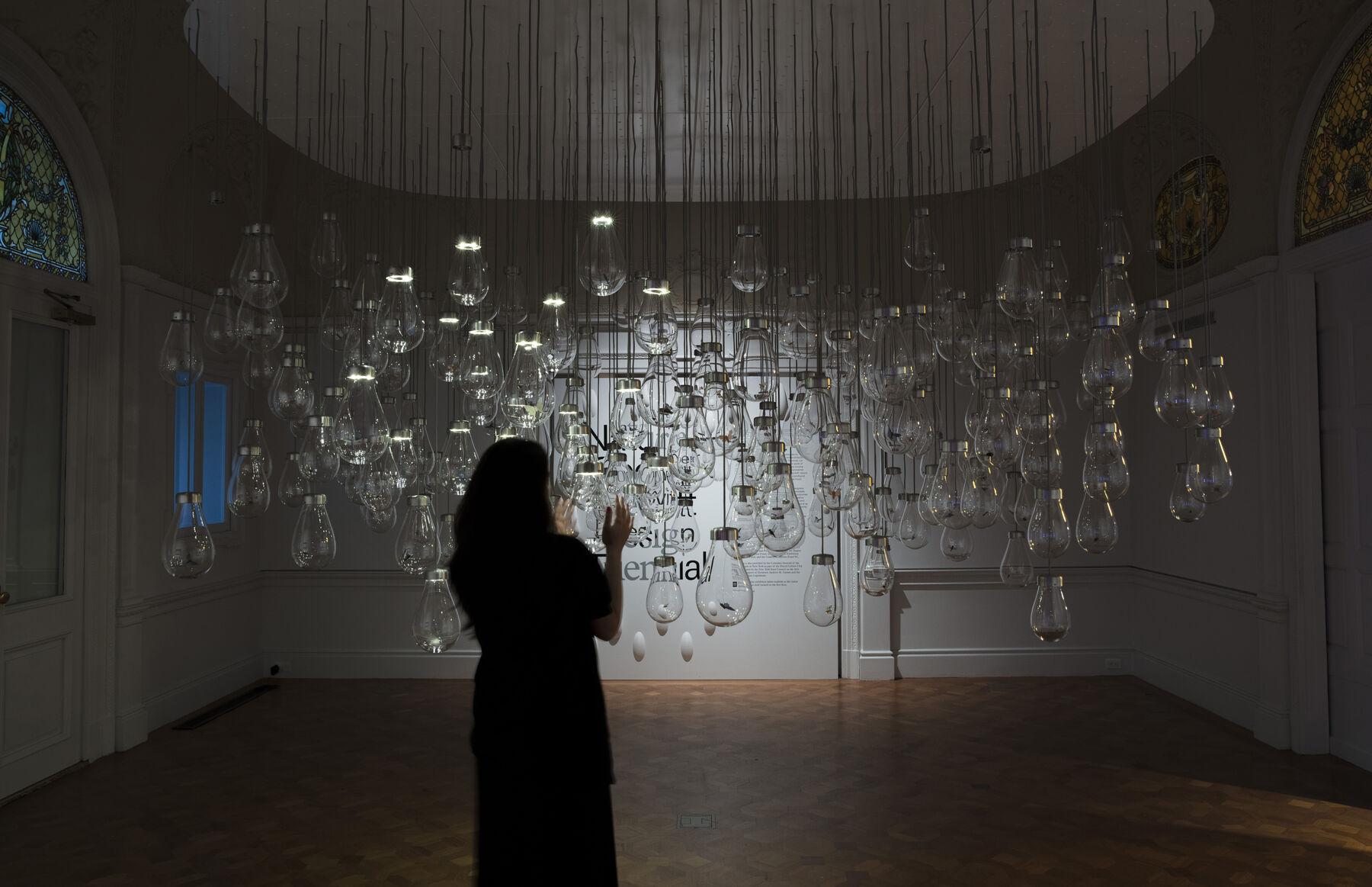 A woman standing in front of a group of blown glass bulbs while carefully having her hands wrapped with one