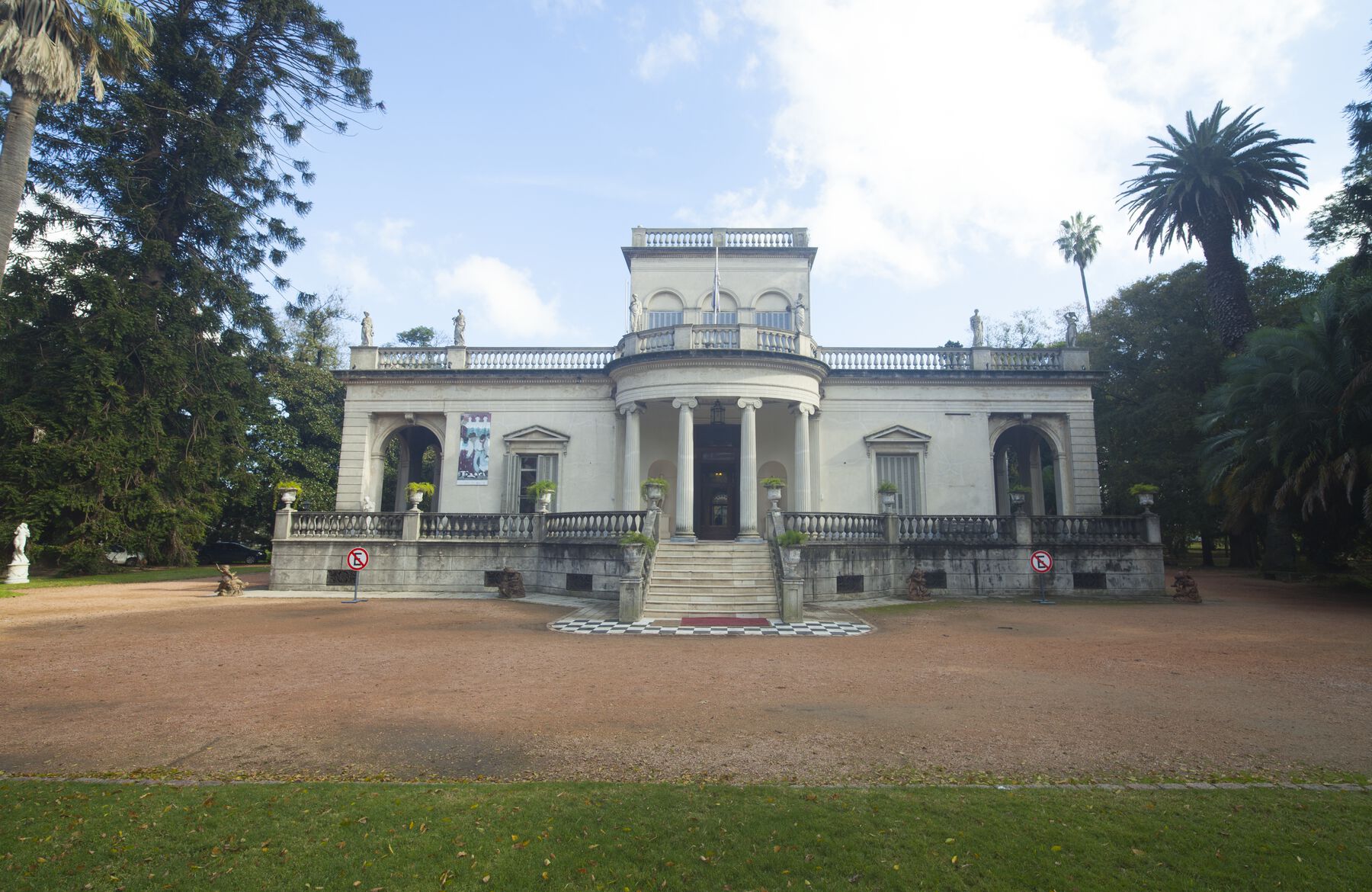 A white building structure with a stairway leading to the door with 4 pillars at front