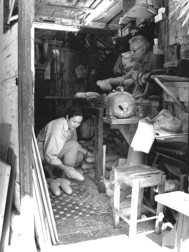 View of workshop from doorway; artist under table inspects rolls while man above looks on