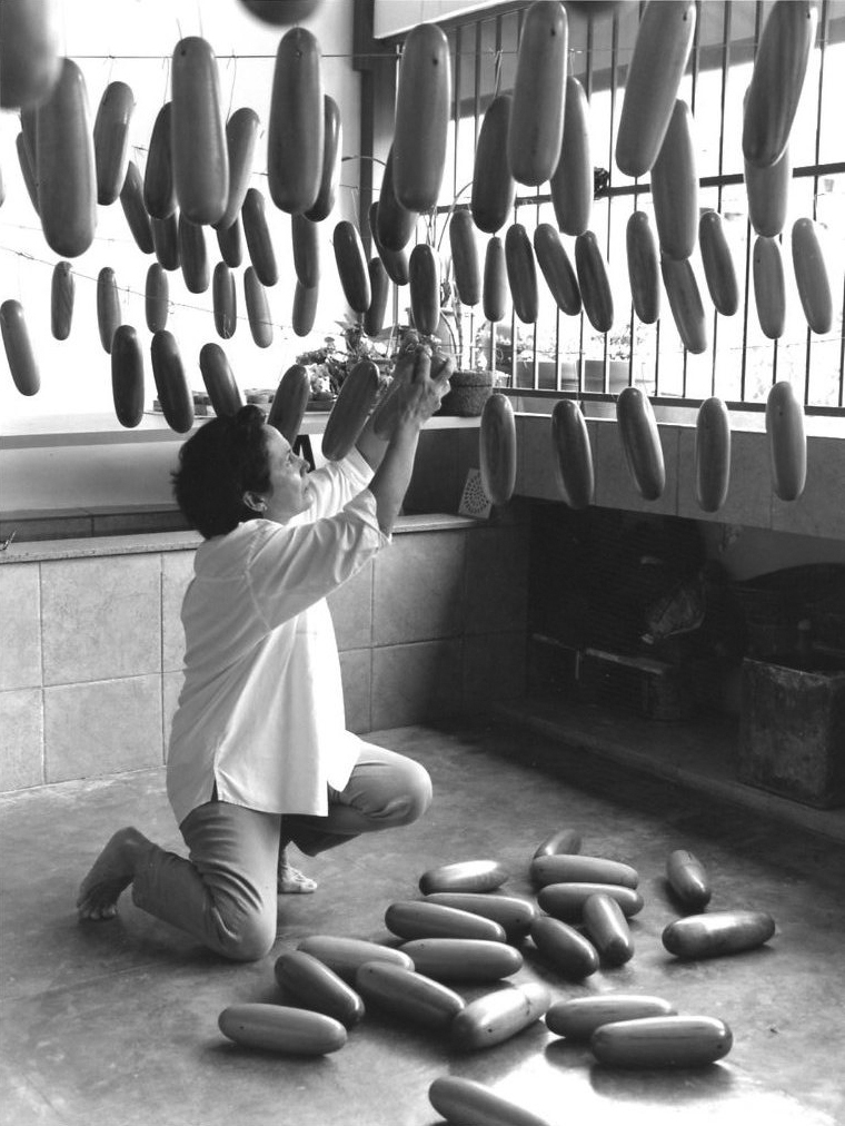 Artist kneeling in corner of sunlit room and suspending rows of wooden rolls from clotheslines