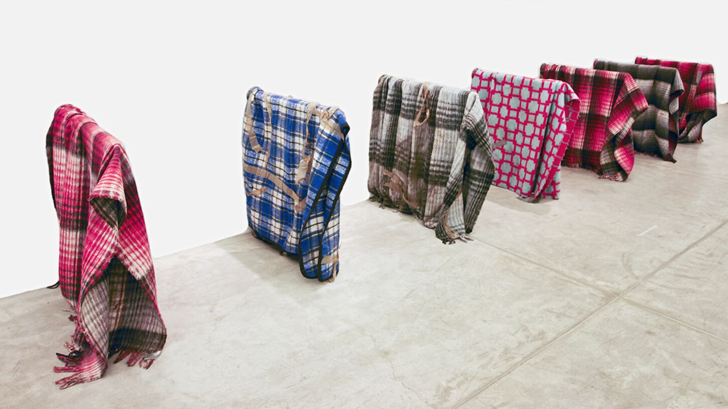 Three-quarter view of row of patterned red, blue, and plaid blankets standing upright in rectangular formations 