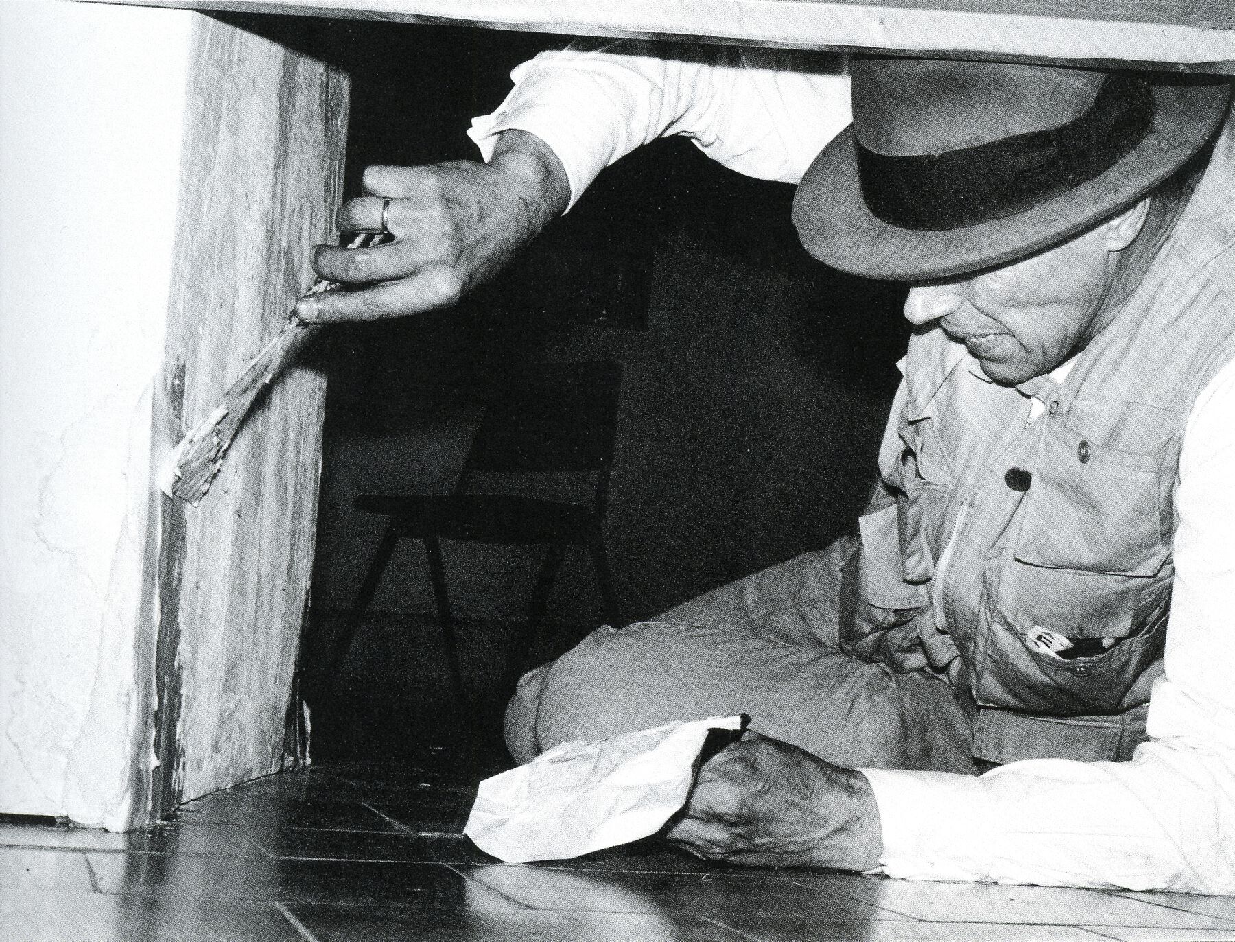 Artist crouching in narrow space to apply butter with a paintbrush, clutching tissue in the other hand