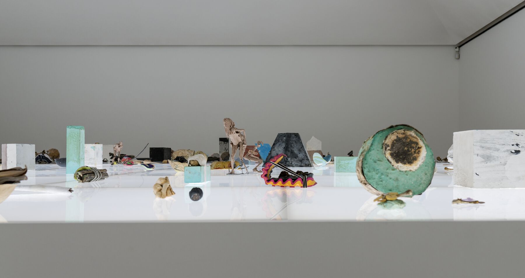 Assorted objects, including a geode, figurative sculptures, glass blocks, placed on a bright white surface