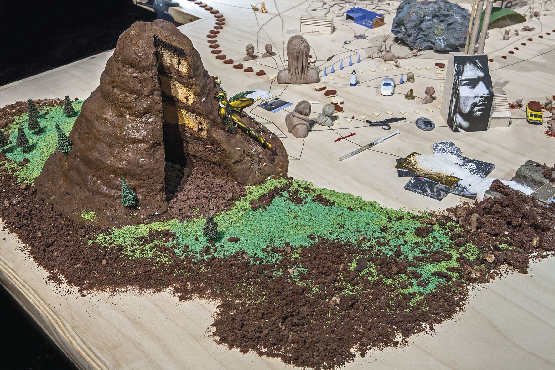 Modelled brown-and-green hill-scape on workshop table with tools and miniature model parts on the right